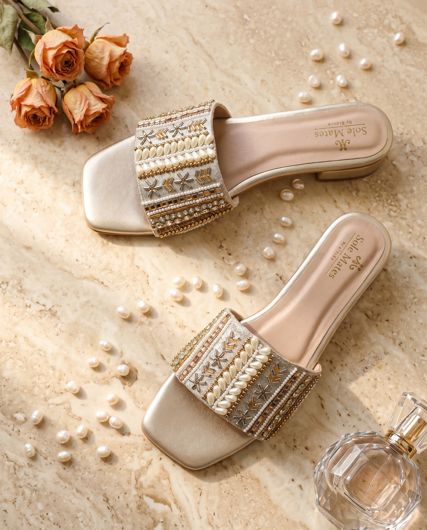 Kate Gold Sliders flat lay on marble with scattered pearls, roses and perfume — champagne gold pearl and bead embellished bridal sliders by Solemates by Palak
